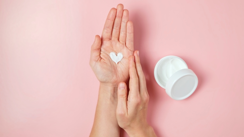 Flatlay of a gentle ADHD skincare routine setup with a heart-shaped cream dollop and open jar on a pink background